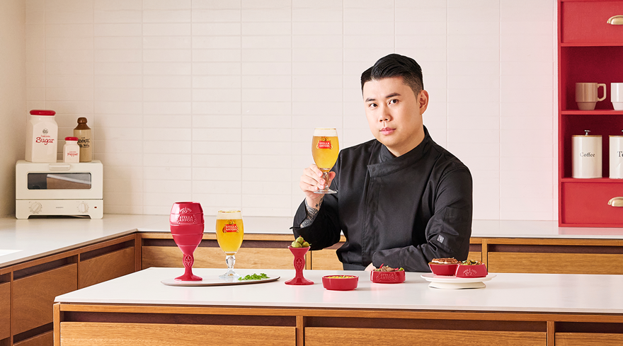 쉐프 나폴리 맛피아가 스텔라 아르투아 챌리스에 채워진 맥주를 들고 있으며, 고메 챌리스에 음식이 담겨 있습니다.