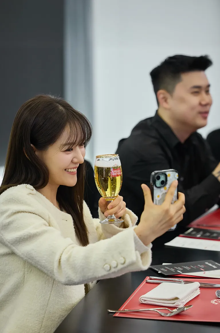 박은영 셰프가 한 손에 스텔라 아르투아 생맥주를 들고 다른 손으로 휴대폰 셀피를 찍으며 밝게 웃고 있습니다