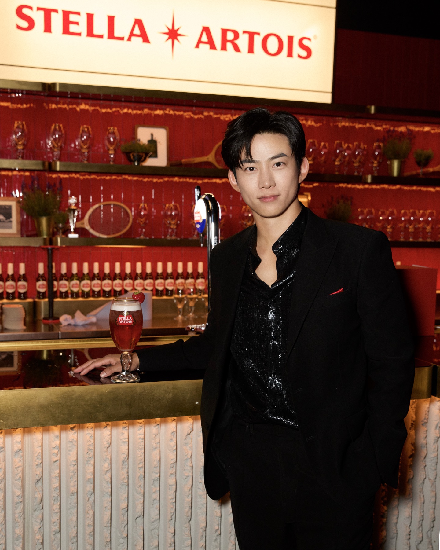 검정 정장을 입은 옥택연이 붉은 인테리어의 스텔라 아르투아 바 앞에 서 있고, 바 위에 챌리스 생맥주가 놓여 있다.