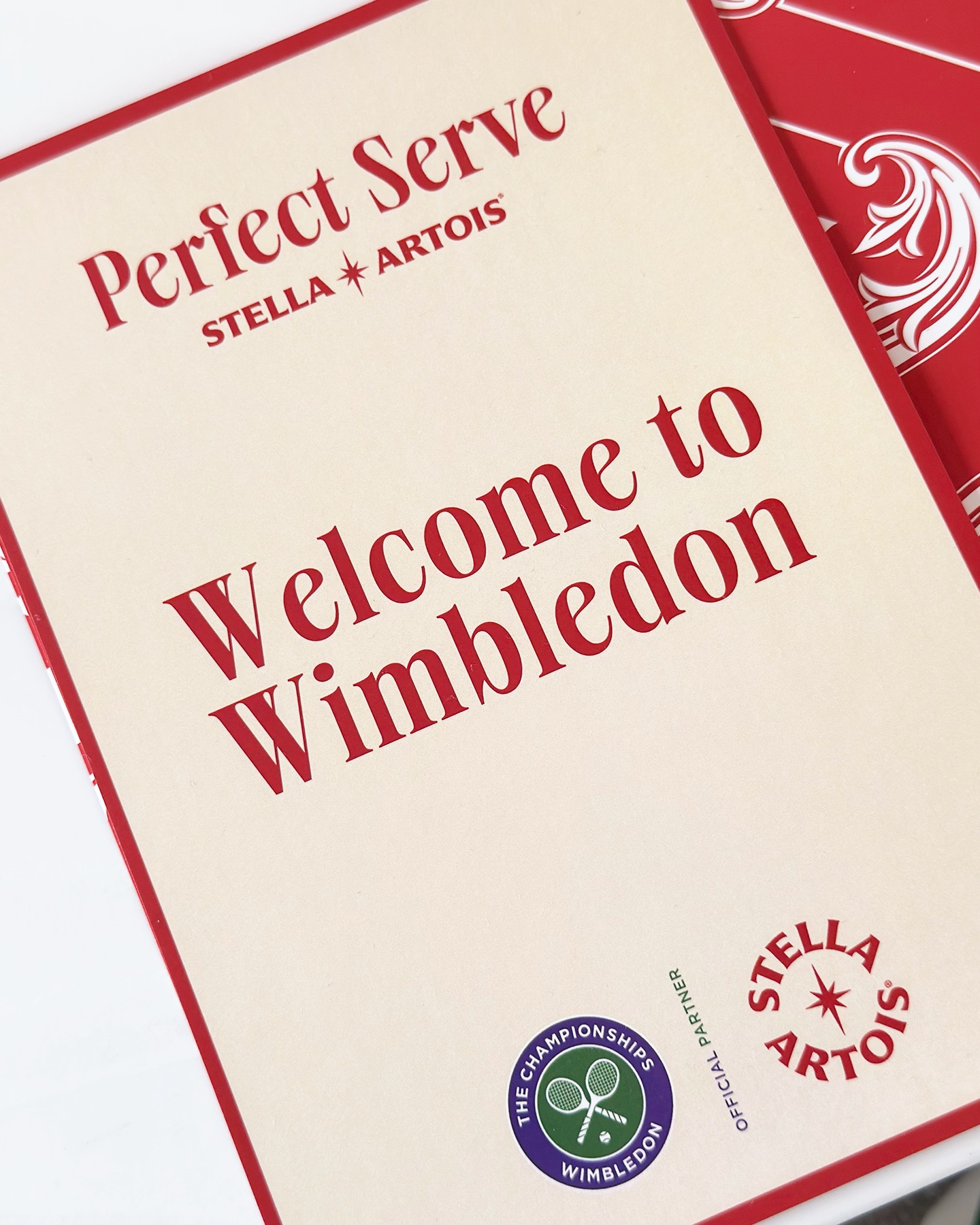 'Perfect Serve - Stella Artois'와 'Welcome to Wimbledon'이 적힌 웰컴 카드. Wimbledon 공식 파트너 로고와 스텔라 아르투아 로고가 함께 있다.