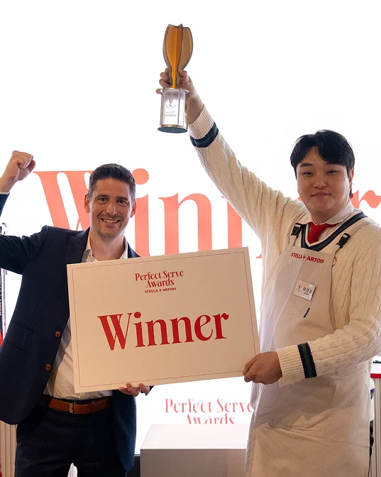 우승자가 챌리스 트로피를 들어올리고 옆에서 'Winner' 보드를 든 동료와 함께 환호하고 있습니다